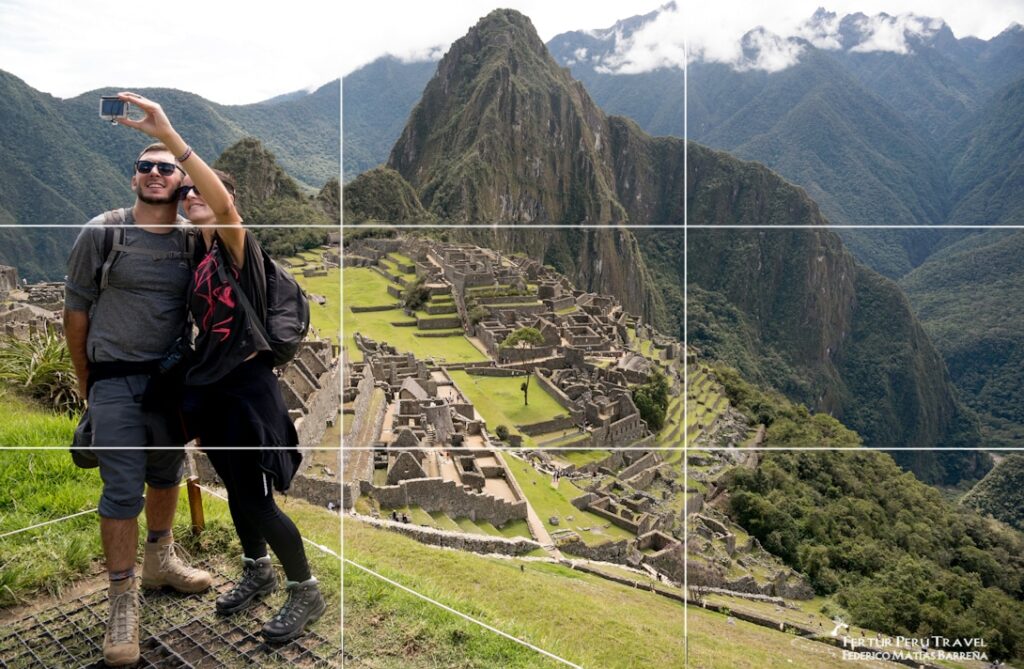 Pareja tomando selfie en Machu Picchu con cuadrícula de regla de los tercios superpuesta, demostrando técnicas de composición fotográfica en las ruinas incas del Perú con Huayna Picchu de fondo