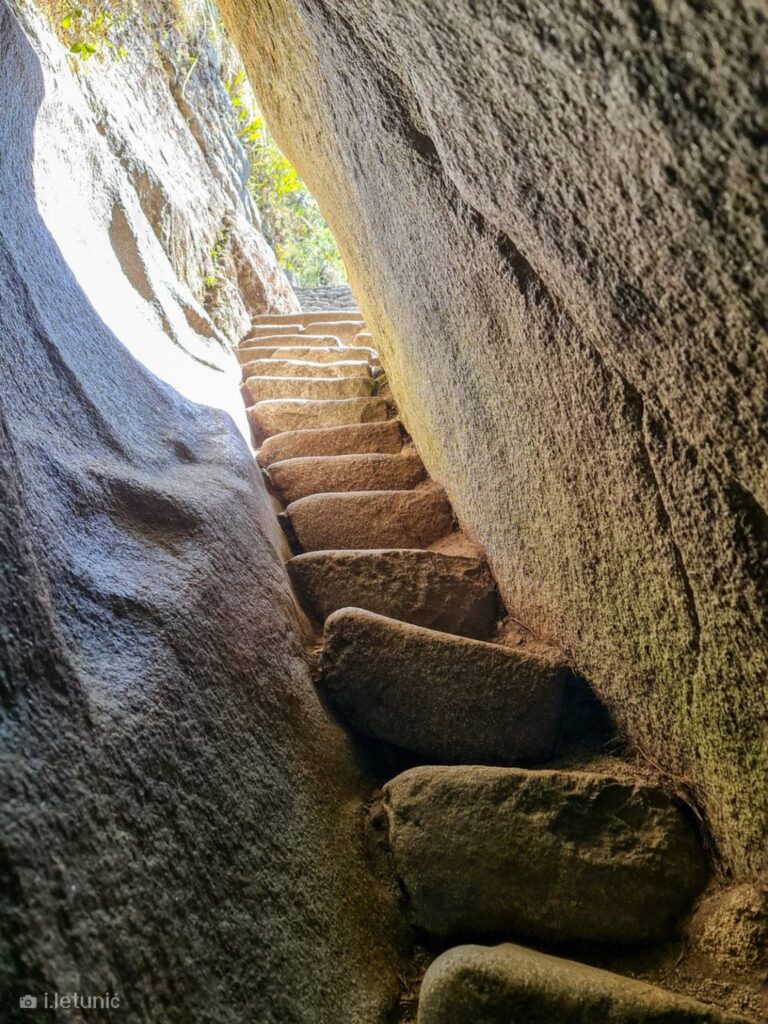 Escalera de piedra inca en túnel antiguo de Huayna Picchu con luz natural filtrándose, arquitectura original inca en Machu Picchu, fotografía de bajo nivel de luz por Ivica Letunic